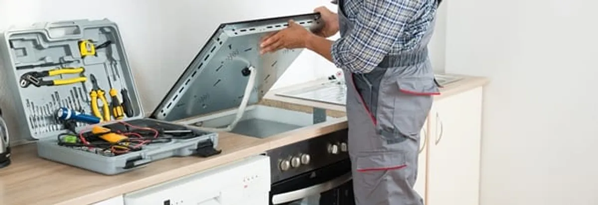 Cooktop repair technician lifting a built-in stovetop for service in Columbia, SC
